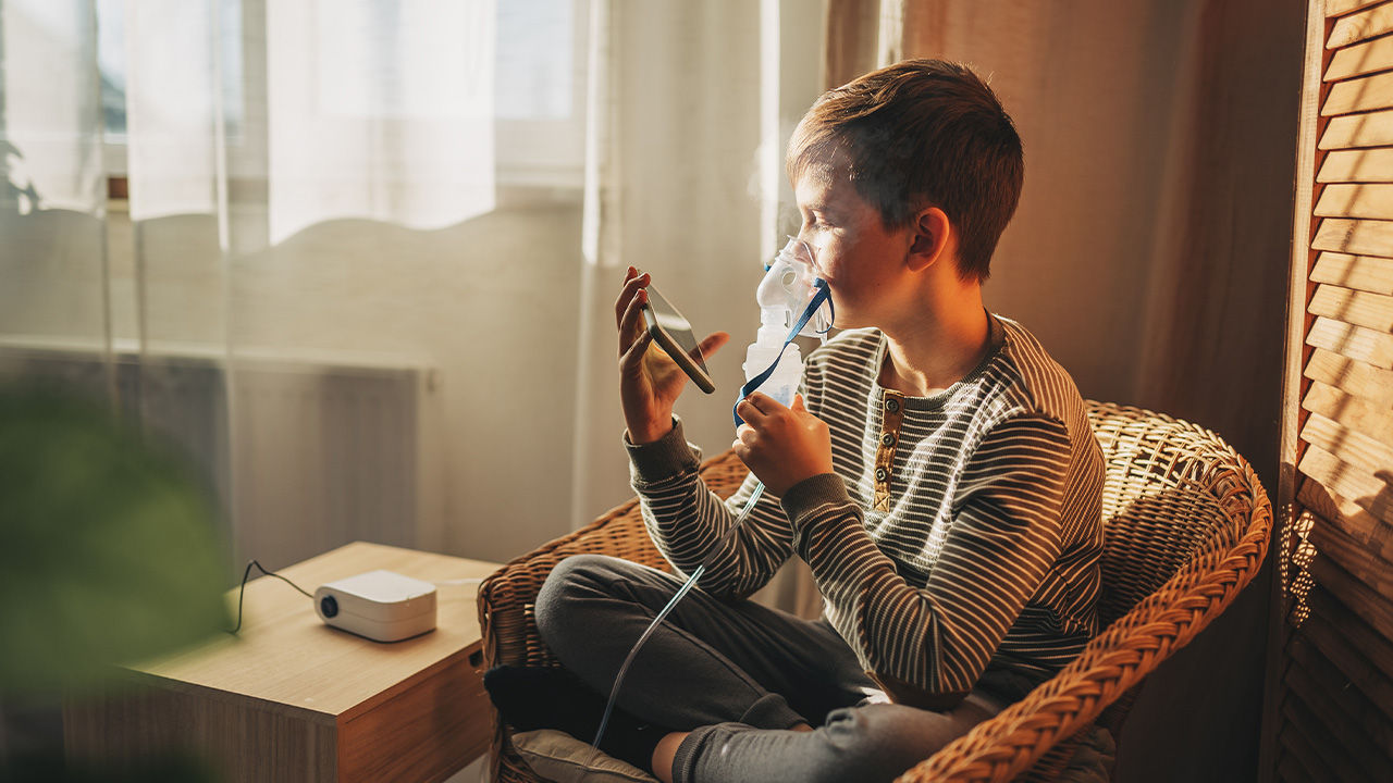 A young child uses a handheld respiratory therapy at home.