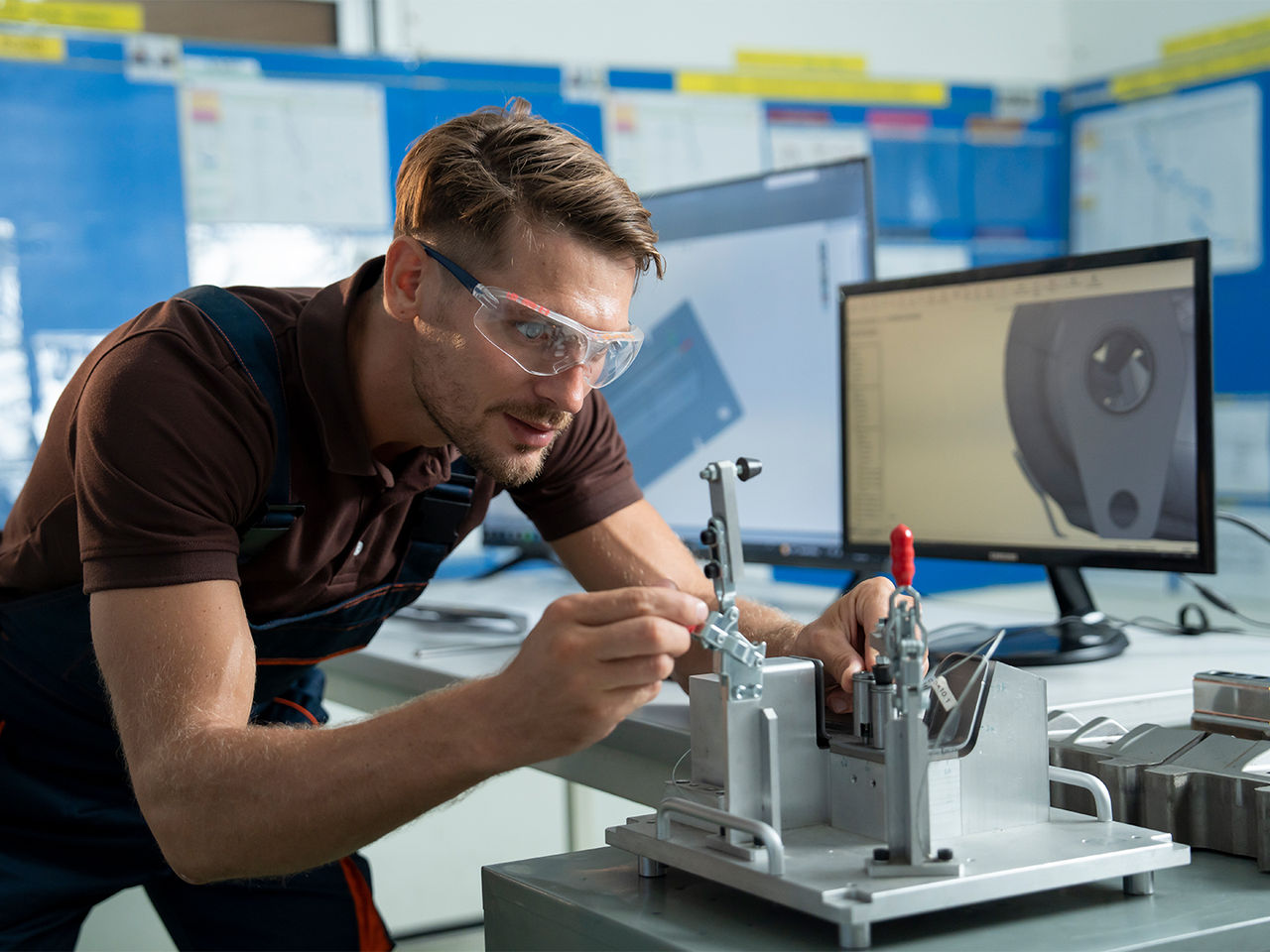 Engineer adjusts a component in a test fixture with a CAD model displayed on a nearby computer screen.