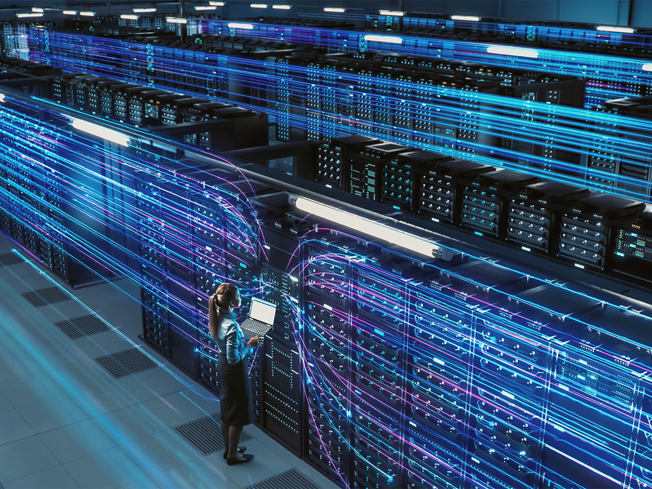 IT professional using a laptop in a modern data center with glowing blue server racks.