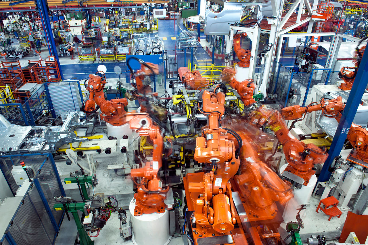 Orange robotic arms operate inside an automated industrial assembly line.
