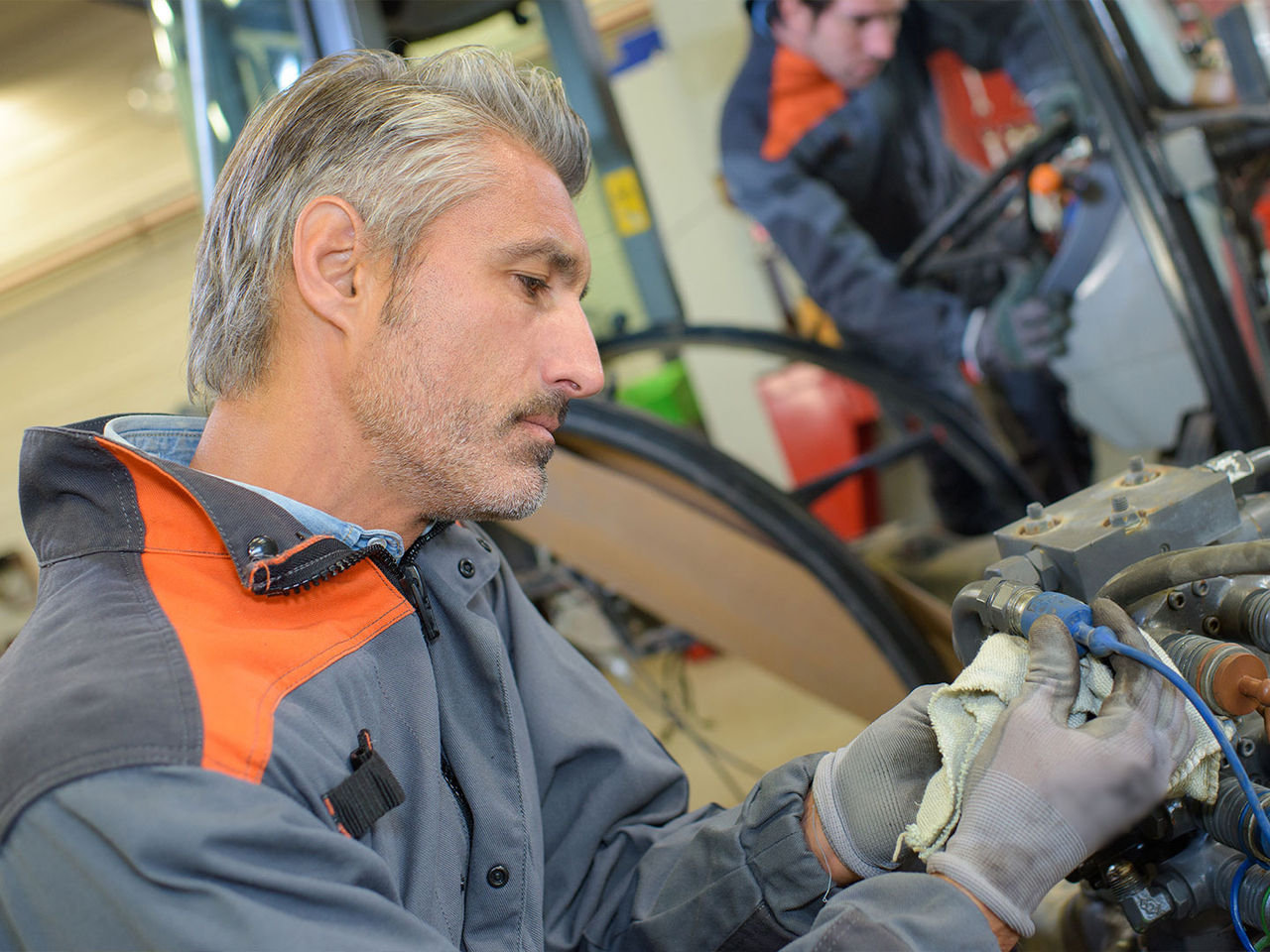 Mechanic manually connecting wires in a tractor engine.