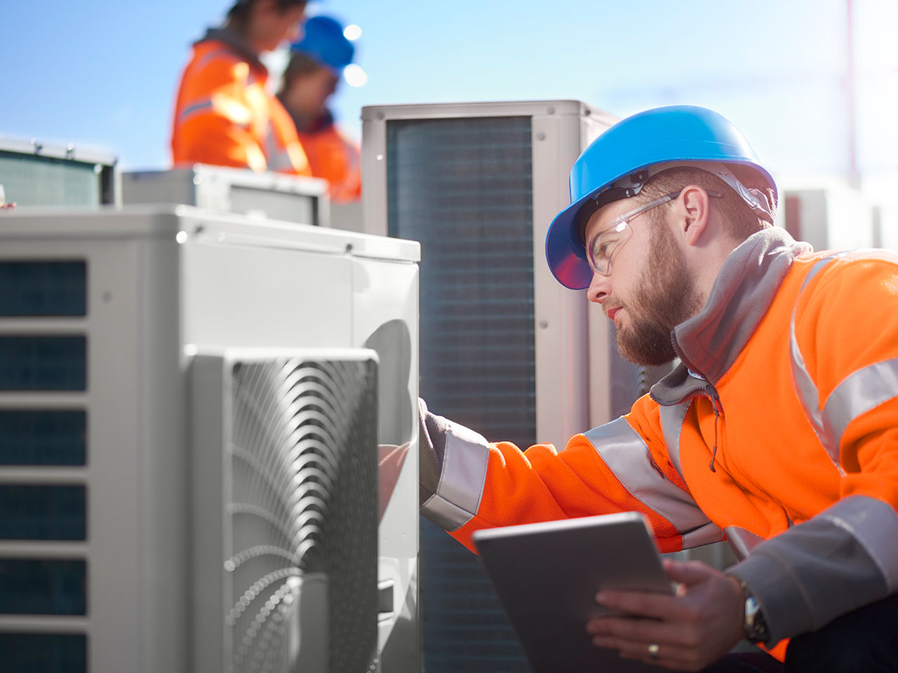 Technician in safety gear inspecting an outdoor HVAC unit. 